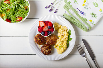Turkey burgers with scrambled eggs and berries on white wooden background. High angle view, top studio shot