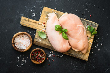 Raw chicken meat at wooden board with spices at black background. Flat lay with copy space.