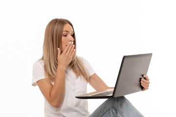 Surprised young woman with long hair looks at her laptop while seated casually, expressing shock or...