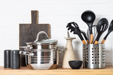 Kitchen table, kitchen utensils, cooking pots with wooden cutting board, white modern interior.