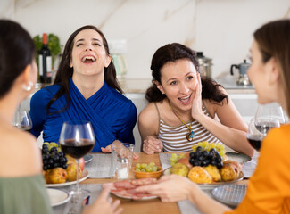 Four women friends are sitting at table, enjoying food and wine, chatting, talking, laughing. In homely atmosphere, adult class fellow friends celebrate anniversary