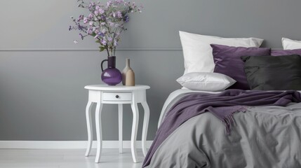 Sleek bedroom showcasing a white side table, royal purple decor items, charcoal grey bedding, and minimalist ambiance.