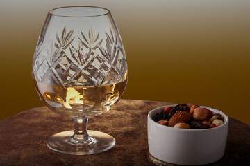 Large brandy in a brandy glass with a bowl of nuts at the side.
