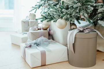 Decorated Christmas tree stands in sunlit living room, adorned with golden ornaments and twinkling lights. Wrapped presents, gift boxes under Christmas tree, festive atmosphere of winter holidays