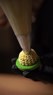 Pastry chef adds cream using a cooking bag to the finished green macaron halves