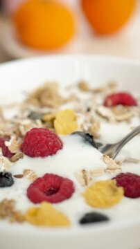 Vertical: the spoon takes fresh milk yogurt from the bowl along with the berry of raspberries and blueberries with the addition of natural granol and oats and corn flakes. Healthy healthy breakfast