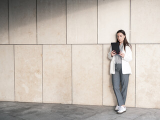 Businesswoman checking tablet while leaning against a modern stone wall
