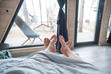 The feet of a married couple sticking out from under the blanket in a country house with panoramic...