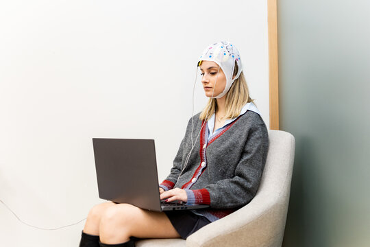 A pretty girl is sitting in a psychology office while interacting with a laptop and undergoing transcranial direct current stimulation. TDCS concept.