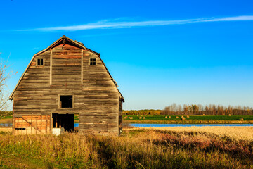 A large, old barn sits in a field with a blue sky overhead