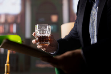 CIA enforcement agent sharing crucial insights to his colleague, enjoying glasses of whiskey in the safe house library. Government spies meeting over drinks to discuss evidence analysis. Close up.