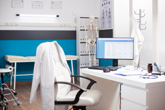 Empty medical office with no people inside, having clinical equipment and computer ready for healthcare use. Modern desktop pc in vacant hospital room displaying patient diagnostic data.