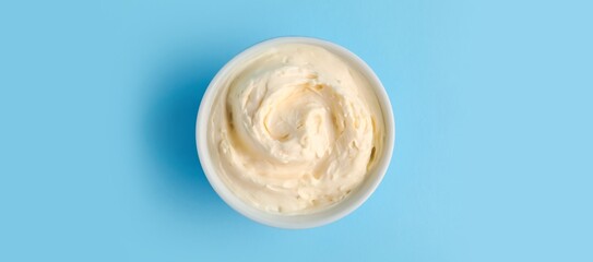 Bowl with tasty cream cheese on blue background, top view
