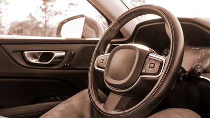 Black leather car steering wheel with a view of the road through the windshield. Colour of the year Mocha Mousse.