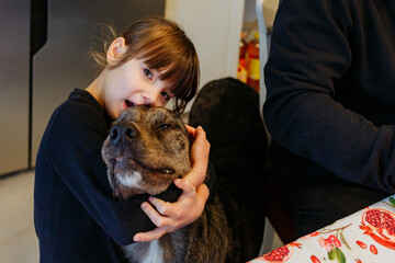little child hugs the dog standing next to the table in the kitchen