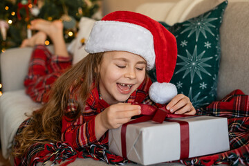 Cute happy little girl opening presents near Christmas tree. Winter holidays.