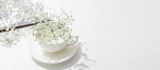 Cup with gypsophila flowers on light background with space for text