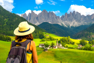 Tourist hiking in the dolomites admiring the funes valley and st. Magdalena church