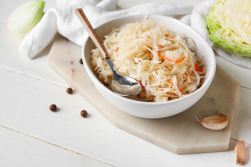 Bowl with homemade sauerkraut, ingredients and stone tray on white wooden background, closeup