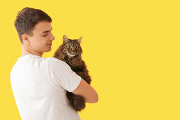 Young man holding cute cat on yellow background