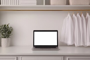 Modern minimalist home office setup featuring laptop with blank screen, potted plant, and white shirts