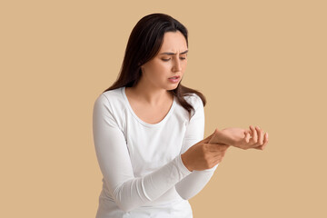 Young woman suffering from pain in wrist on beige background