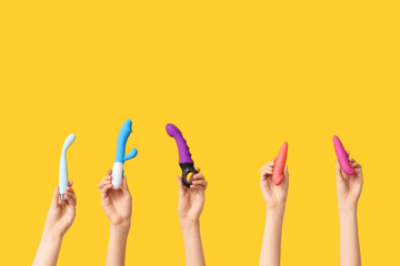 Female hands with different vibrators on yellow background