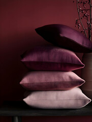 A stack of decorative pillows in varying shades of purple and pink against a dark background.