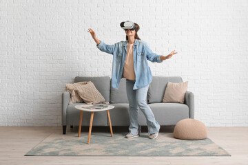 Young beautiful woman in VR eyeglasses near grey sofa at home