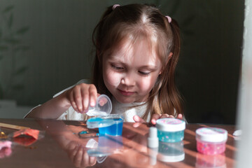 A six-year-old girl stirs blue glue in a container and smiles, creative play, educational circle....