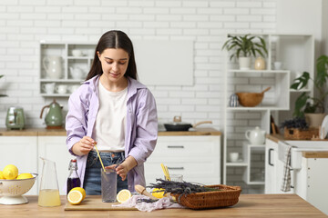 Beautiful young woman with glass of fresh lavender lemonade at table in kitchen
