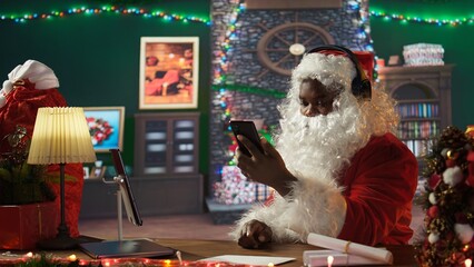 African american Saint Nick listening to Christmas carols and music on smartphone, white bearded...