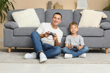 Happy father with his little son playing video games on floor at home