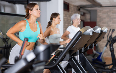Focused motivated young girl leading healthy active lifestyle doing cardio workout in gym, running...