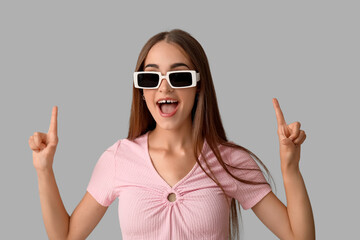 Young woman in sunglasses with diastema pointing at something on light background