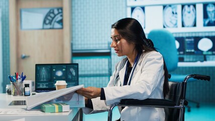 Indian female physician with disability consulting a patient in office, recommending treatment and recovery plan at the hospital. General practitioner meeting with young man. Camera A.