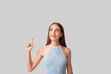 Young woman with diastema pointing at something on light background