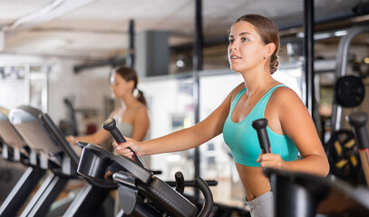 Fototapeta premium Young sporty girl working out on elliptical machine in gym. Healthy active lifestyle concept