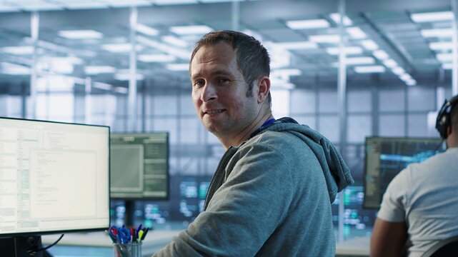 Portrait of smiling engineer inspecting server rows in data center. Happy man supervising supercomputers providing processing and memory resources for various workloads, camera A