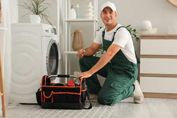 Male plumber with bag of tools fixing washing machine in bathroom