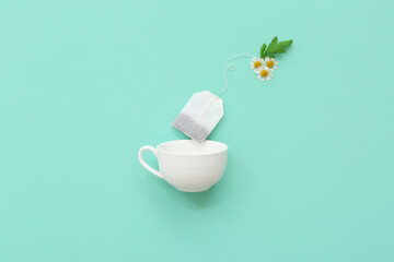 Bag with chamomile tea, flowers and cup on turquoise background. Top view