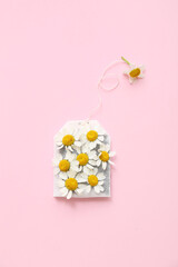 Tea bag and chamomile flowers on pink background. Top view