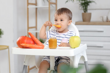 Cute little baby with jar of tasty food, fruit and vegetables eating on chair in kitchen at home