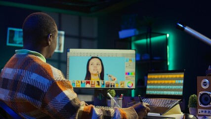 African american photo designer retouching images on dual monitors in a tech driven industry, representing modern digital media. Male graphic artist uses software tools. Camera B.