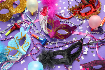 Beautiful carnival masks with balloons, party horns, confetti and beads on lilac background. Top view