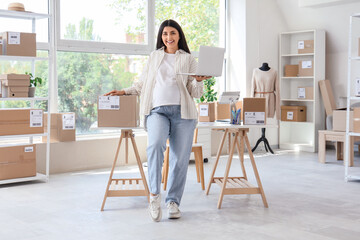 Pregnant seller with laptop and parcel in online store warehouse