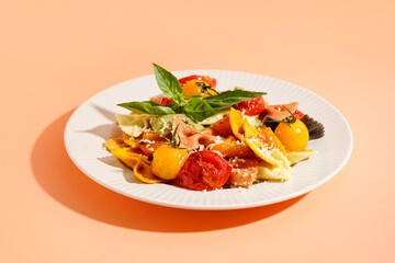 Plate of delicious farfalle pasta with tomato and basil on orange background
