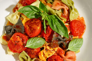 Bowl of delicious farfalle pasta with tomato and basil as background, closeup