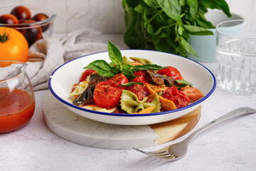 Bowl of delicious farfalle pasta with tomato and basil on light table