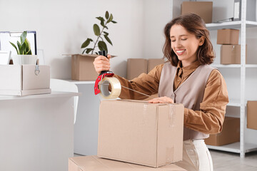 Fototapeta premium Young businesswoman taping box in office on moving day
